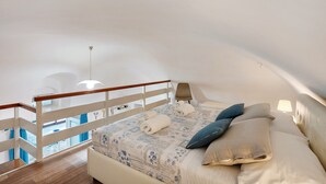 Ein Schlafzimmer mit einem Bett, Kissen, einem Nachttisch, einer Lampe und Blick zum Himmel.