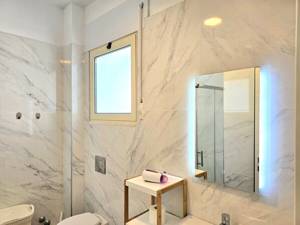 Une salle de bain avec des murs en marbre, une fenêtre, un miroir et un meuble-lavabo en bois.