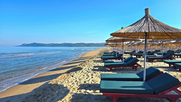 A beach with sun loungers and thatched umbrellas. - Perla Resort (Ishëm)