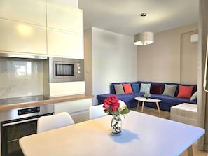 Una cocina moderna con microondas y horno integrados, una mesa de comedor con un florero y un sofá azul con cojines de colores en la sala de estar.