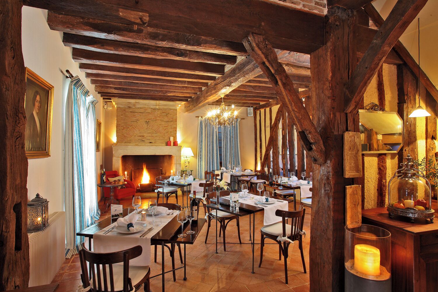 Een restaurant met houten balken, een open haard en gedekte tafels.