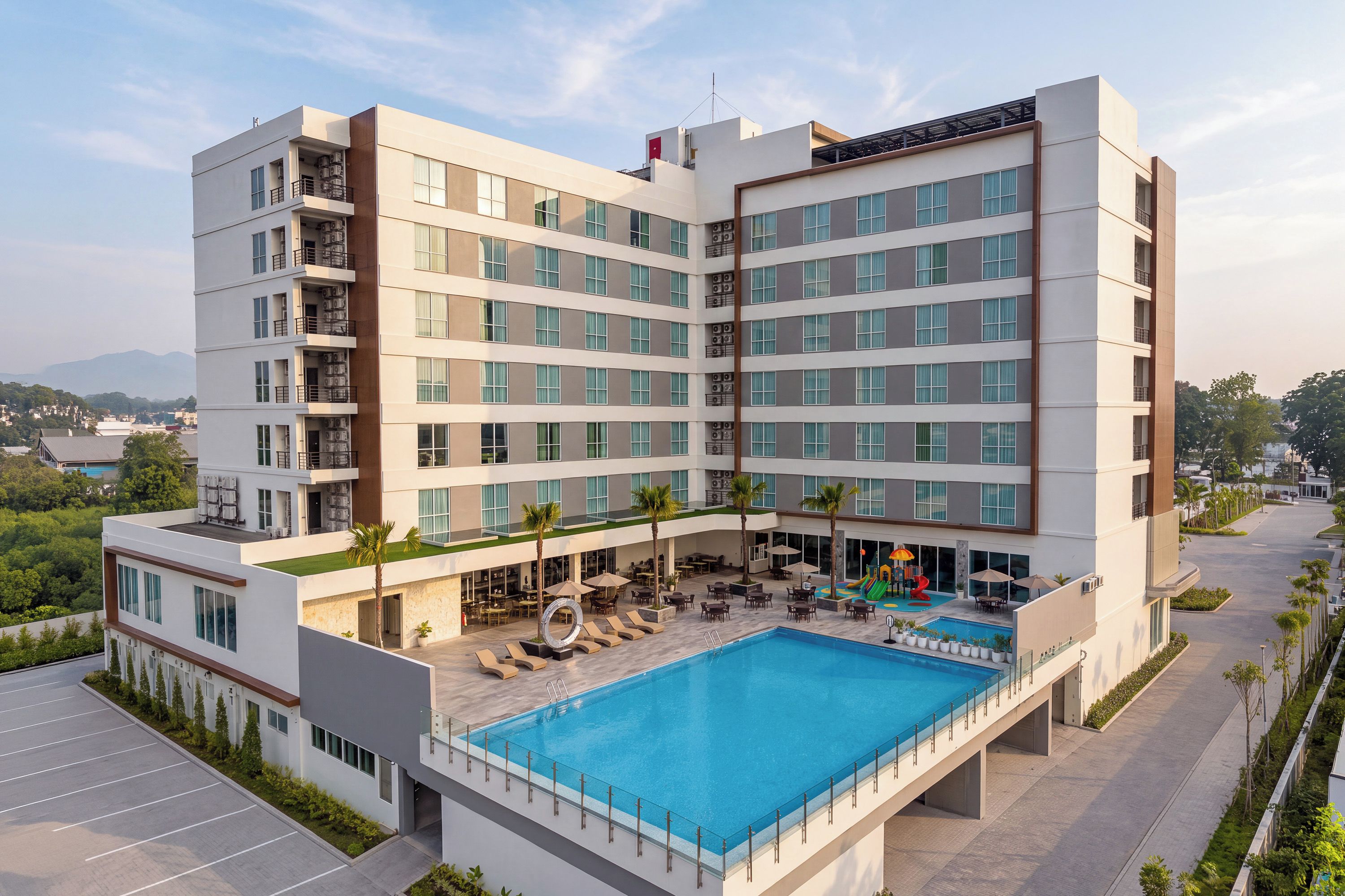 A multi-story hotel with a rooftop pool, outdoor seating, and a view of the surrounding landscape.