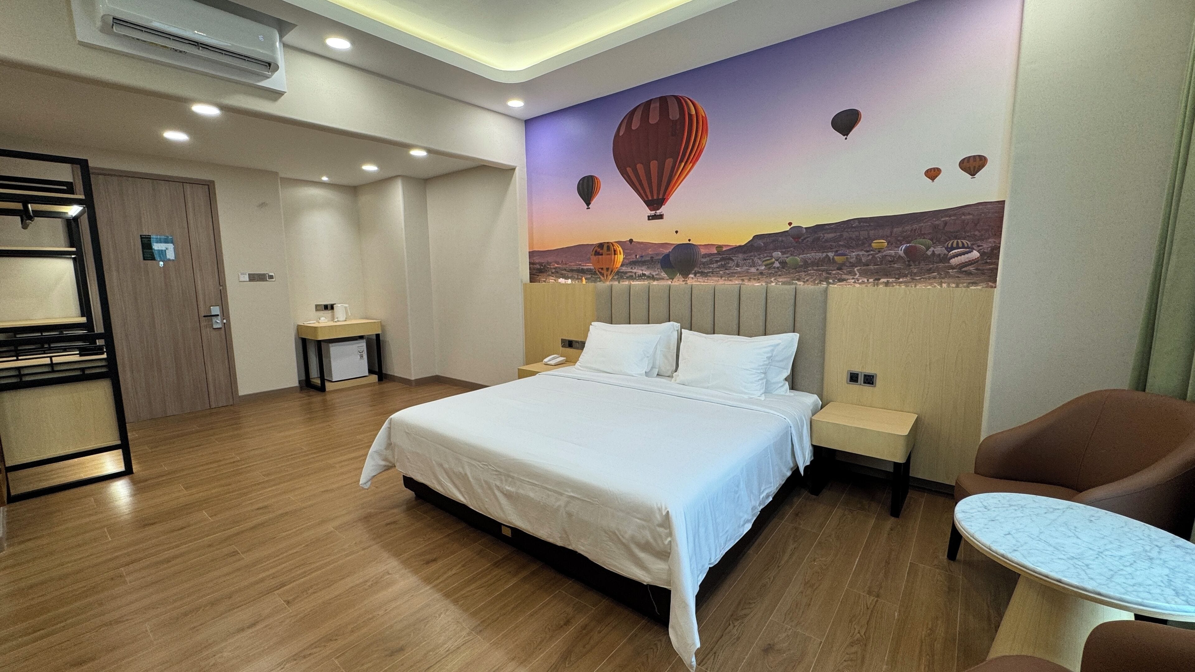 A hotel room with a large bed, a desk, a chair, and a wall mural of hot air balloons.