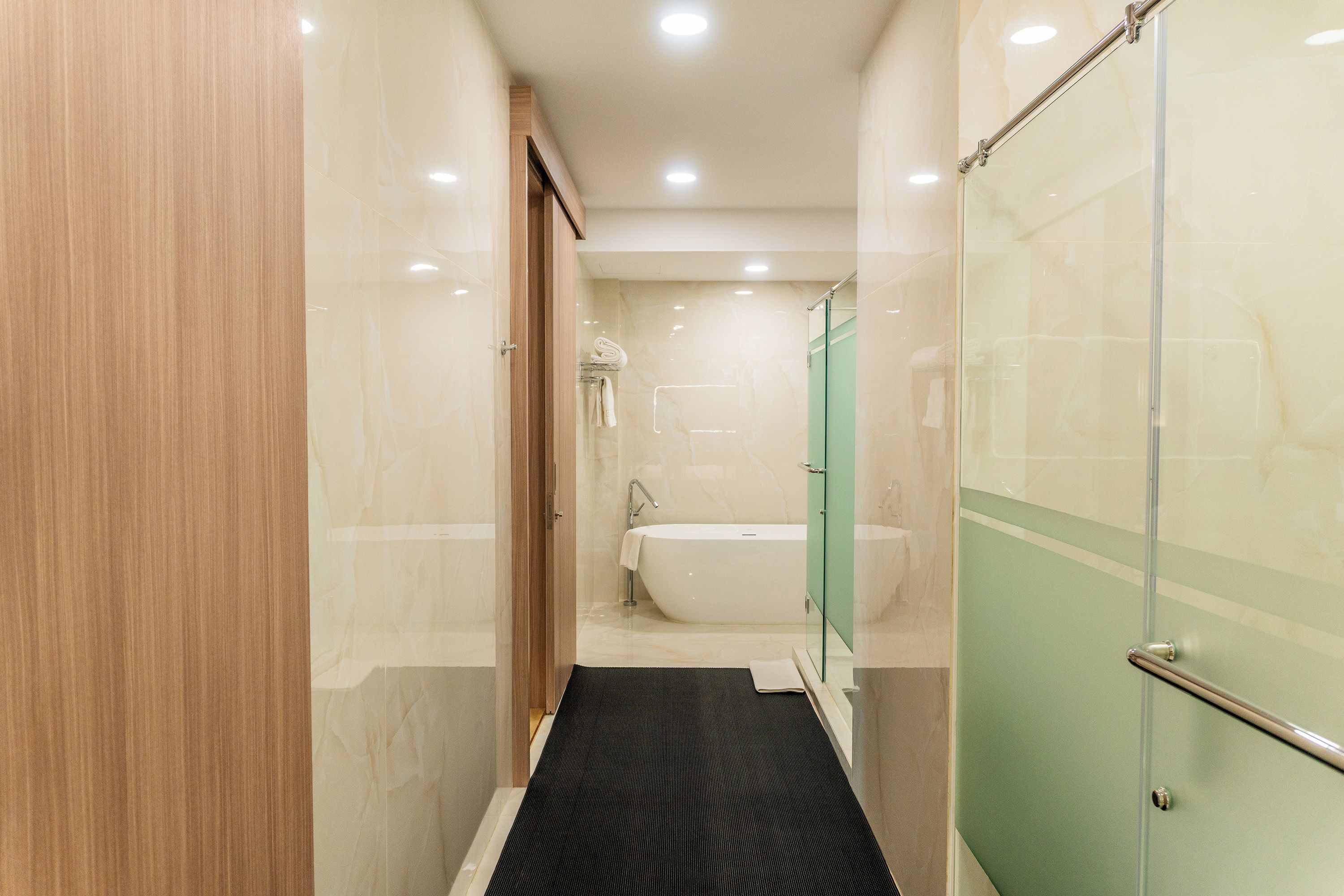 A narrow hallway leading to a bathroom with a bathtub, a glass shower enclosure, and a wooden door.