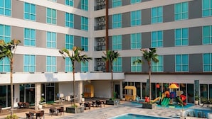 Un hotel con piscina, mobiliario exterior y palmeras.