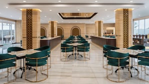 Un moderno hall de hotel con bar central, sillas tapizadas en verde y suelo de mármol.