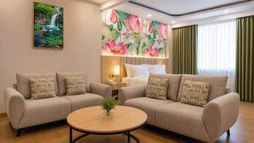 A hotel room with two sofas, a round coffee table, a painting of a waterfall, and a floral mural.