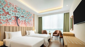 Habitación de hotel con dos camas, un mural floral grande, un televisor, un escritorio y vistas a la ciudad.