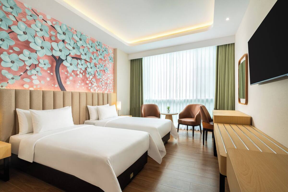Habitación de hotel con dos camas, un mural floral grande, un televisor, un escritorio y vistas a la ciudad.