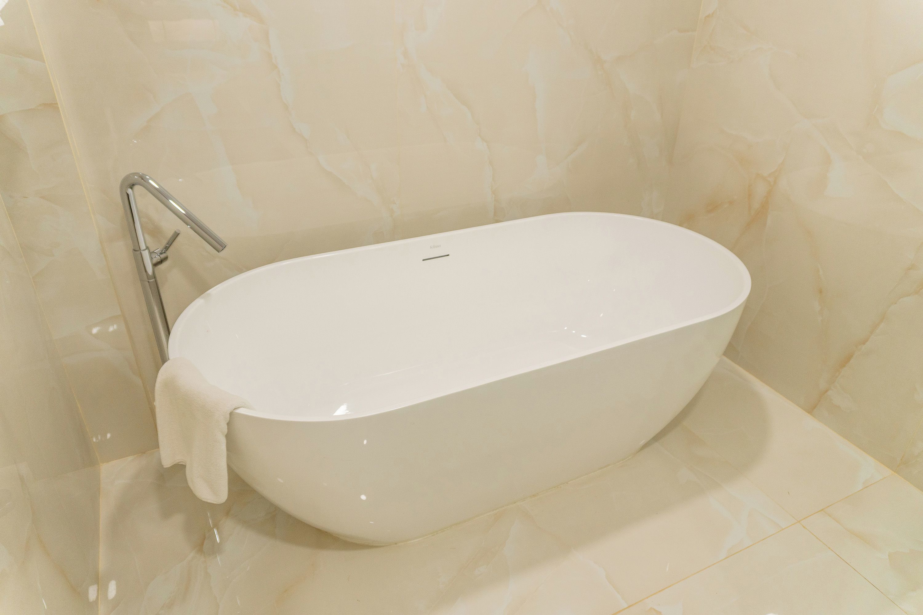 A white freestanding bathtub in a bathroom with a marble wall.