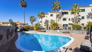 Ein Swimmingpool, umgeben von Palmen und einem Gebäude mit Balkonen.