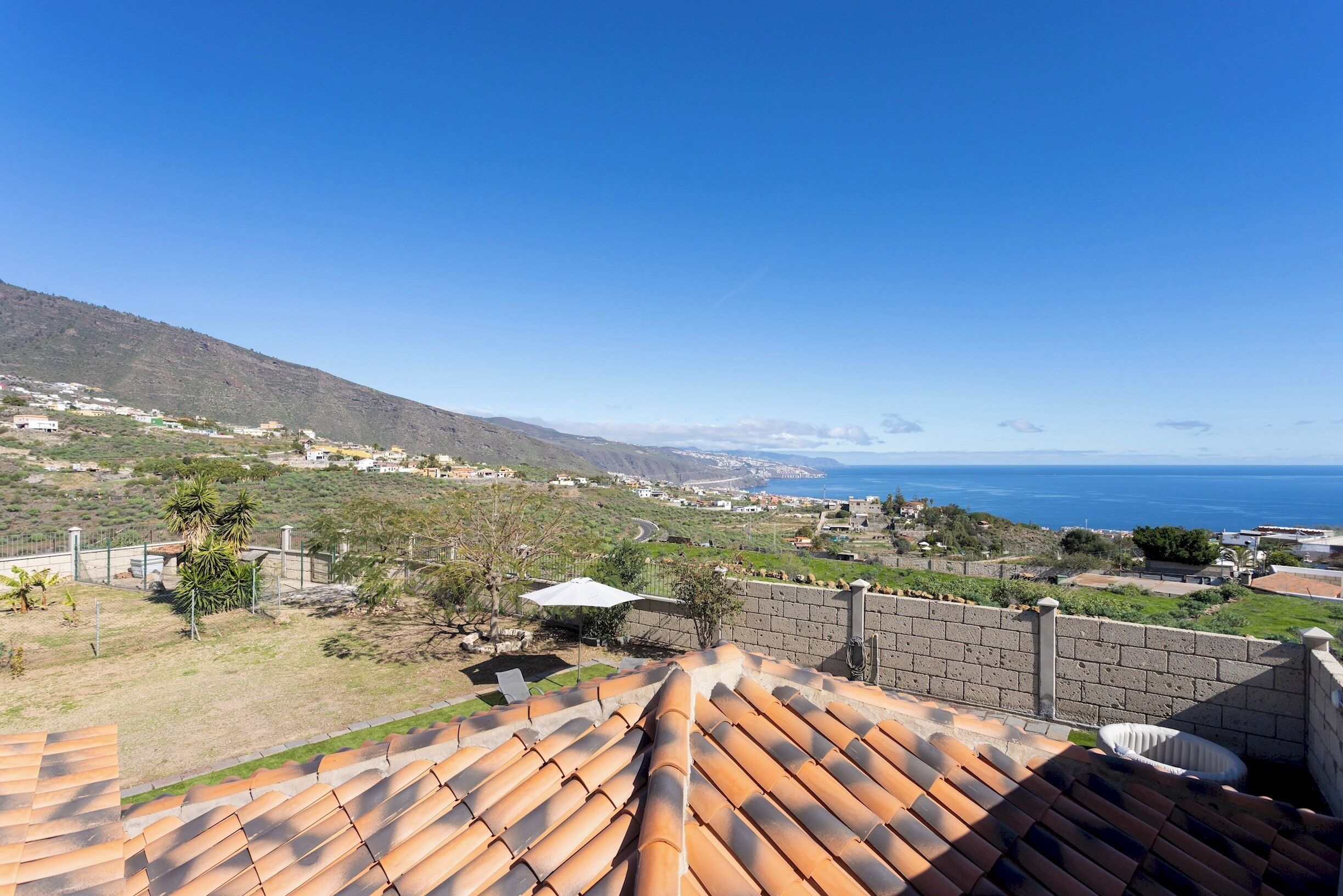 A rooftop terrace with terracotta tiles, a view of the sea, and a distant mountain range.