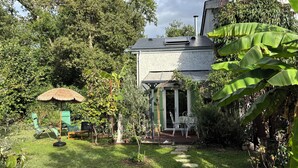 Una casa con jardín, un paraguas de paja y mobiliario exterior.