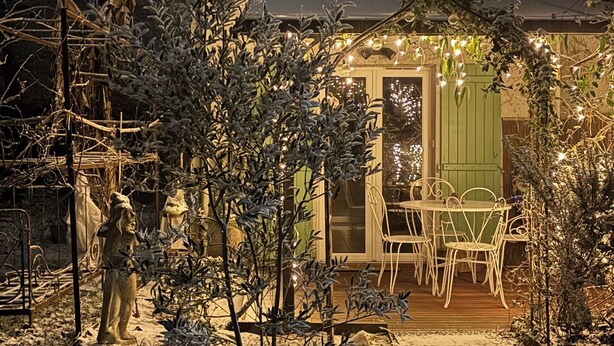 Un espacio exterior cubierto de nieve con una mesa y sillas de patio, rodeado de árboles y una estatua.