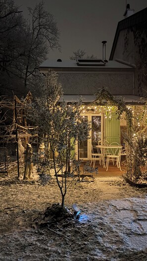 Un espacio exterior cubierto de nieve con una mesa y sillas de patio, rodeado de árboles y una estatua.