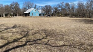 Un extenso campo cubierto de césped con una casa azul que tiene un porche y una chimenea.