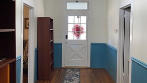 Un pasillo con piso de madera, una puerta blanca con ventana y un aplique colgante.