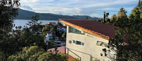 A modern house with a red-tiled roof, a stone exterior, and a view of a lake and mountains in the background.