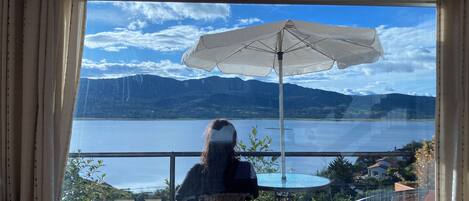 Un balcón con mesa y sillas, una sombrilla y vistas a un lago y montañas.