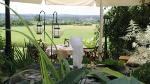 Une terrasse de jardin avec une table et des chaises, un élément décoratif aquatique et des lanternes suspendues.