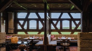 Un espace repas agrémenté de poutres en bois, de grandes fenêtres et offrant une vue sur un paysage verdoyant.