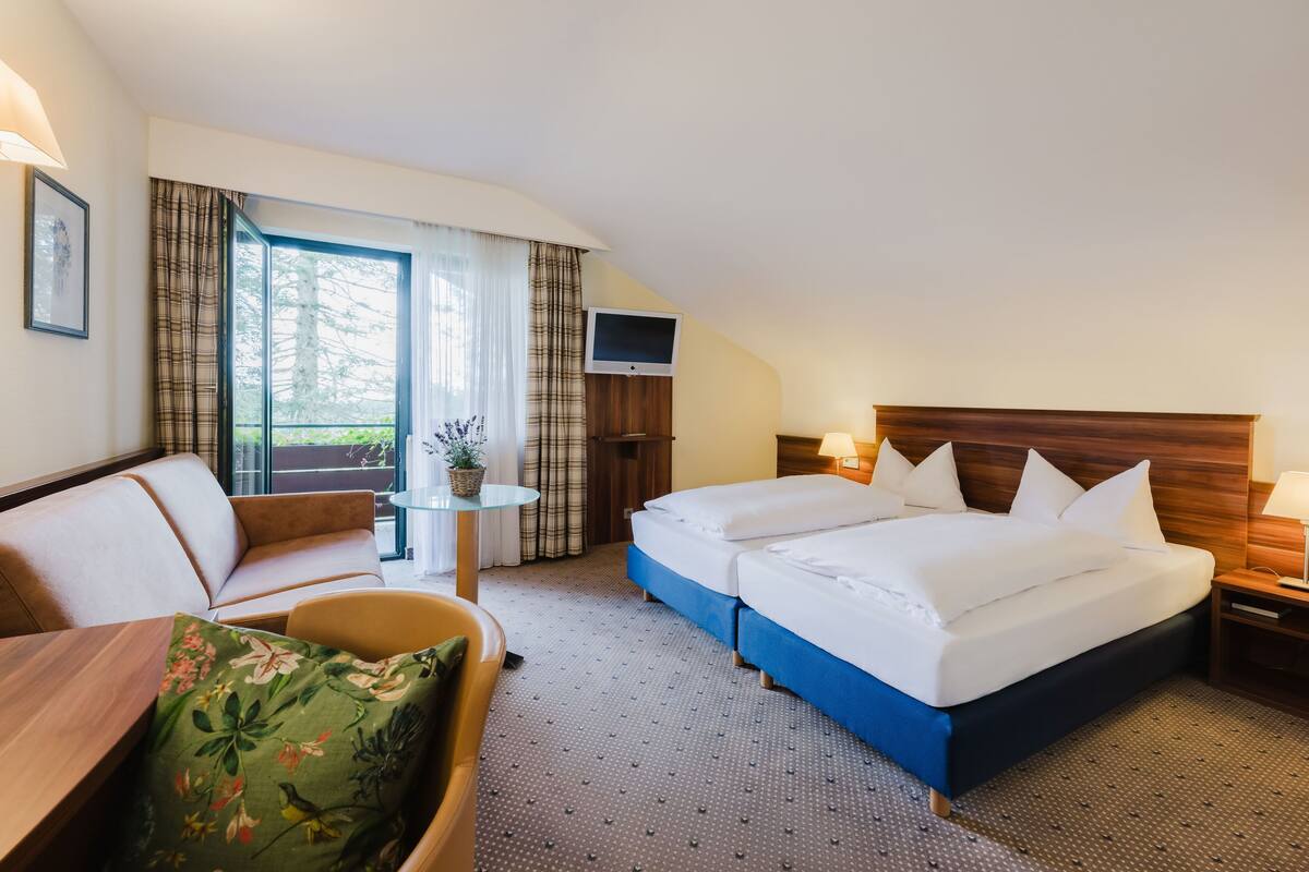 Une chambre d’hôtel avec un lit, un canapé, une petite table, une télévision et une fenêtre avec des rideaux.