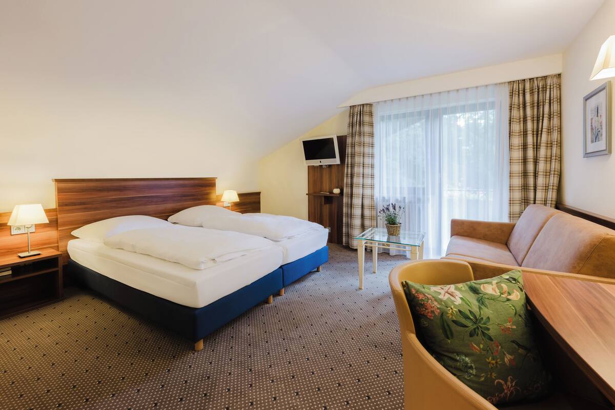 Une chambre d’hôtel avec un lit, un canapé, une télévision et une petite table sur laquelle est posée une plante.
