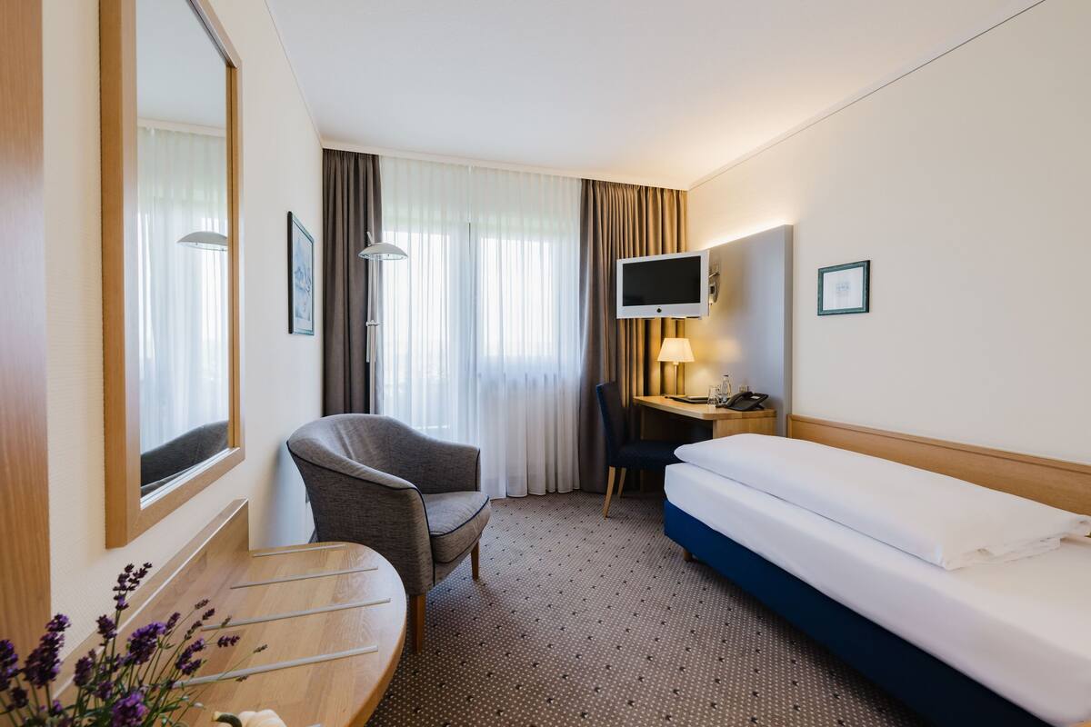 Une chambre d’hôtel avec un lit, un bureau et une chaise, une télévision et une fenêtre avec des rideaux.