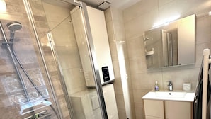 Ein modernes Badezimmer mit einer Duschkabine, einer Toilette und einem Waschbecken mit Spiegel darüber.