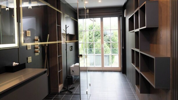 A modern bathroom with a large mirror, a toilet, and a sink. There is a window with a view of greenery outside. - Exclusive designer apartment (Bad Honnef)