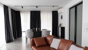 A modern living room with a brown leather sofa, a dining area with a table and chairs, and a large window with black and white curtains. - Exclusive designer apartment (Bad Honnef)