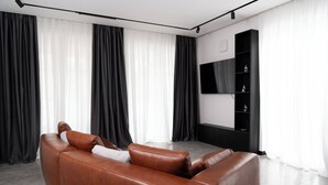 A modern living room with a brown leather sofa, a flat-screen TV mounted on the wall, and a black entertainment unit. - Exclusive designer apartment (Bad Honnef)