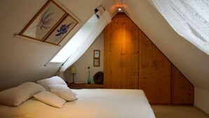 Quarto com teto inclinado, cama com roupa de cama branca e guarda-roupa de madeira.