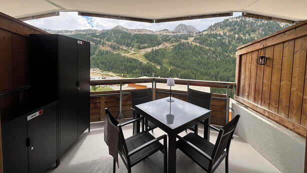 Un balcón con mesa y sillas, un refrigerador y vistas a un paisaje montañoso.