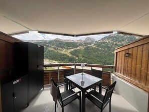 A balcony with a table and chairs, a refrigerator, and a view of a mountainous landscape. - Isola 2000 New (Isola)