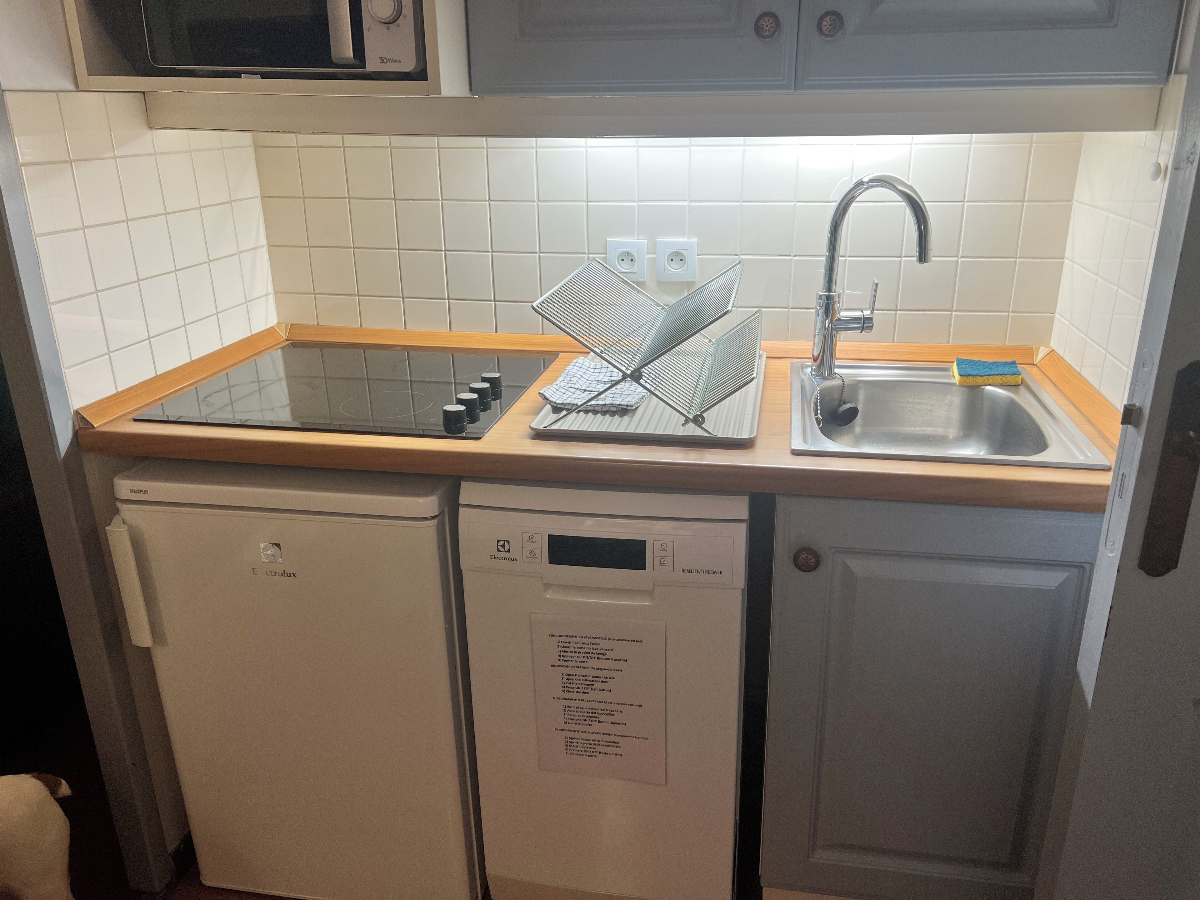 A compact kitchen with a built-in microwave, a sink with a dish rack, and a dishwasher.