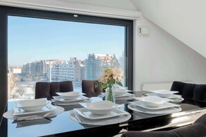 A dining table set for six with a view of city buildings through a large window. - Spacious Apartment | Parking, Air Conditioning, Close to the River (Gdańsk)