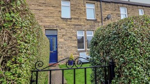 A stone house with a blue door, a satellite dish, and a small garden. - 23 Northumbria Terrace (Morpeth)