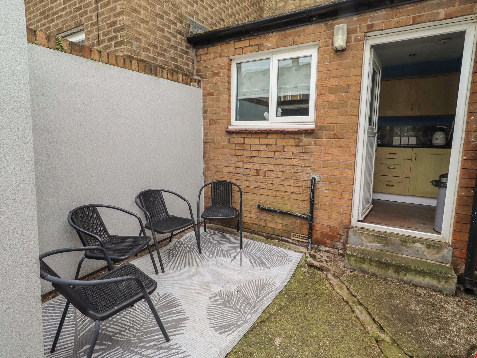 A patio area with three metal chairs and a patterned rug.