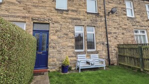 A stone house with a blue door, a small garden with a bench, and a satellite dish. - 23 Northumbria Terrace (Morpeth)
