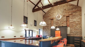 A kitchen with a central island, pendant lights, a stone wall, and a vintage refrigerator. - The Barn at Sunny Barn (Brecon)