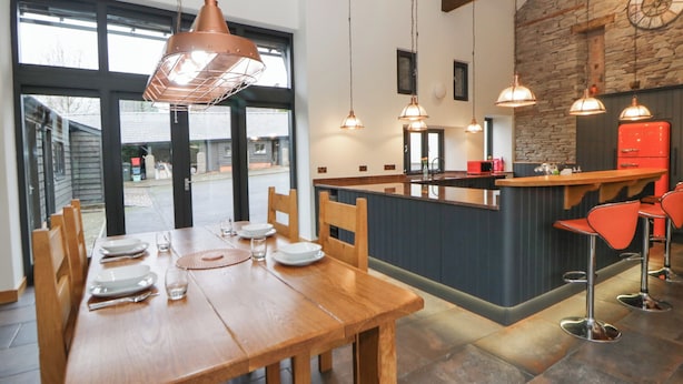 A modern kitchen with a central island, pendant lights, and a stone accent wall. - The Barn at Sunny Barn (Brecon)