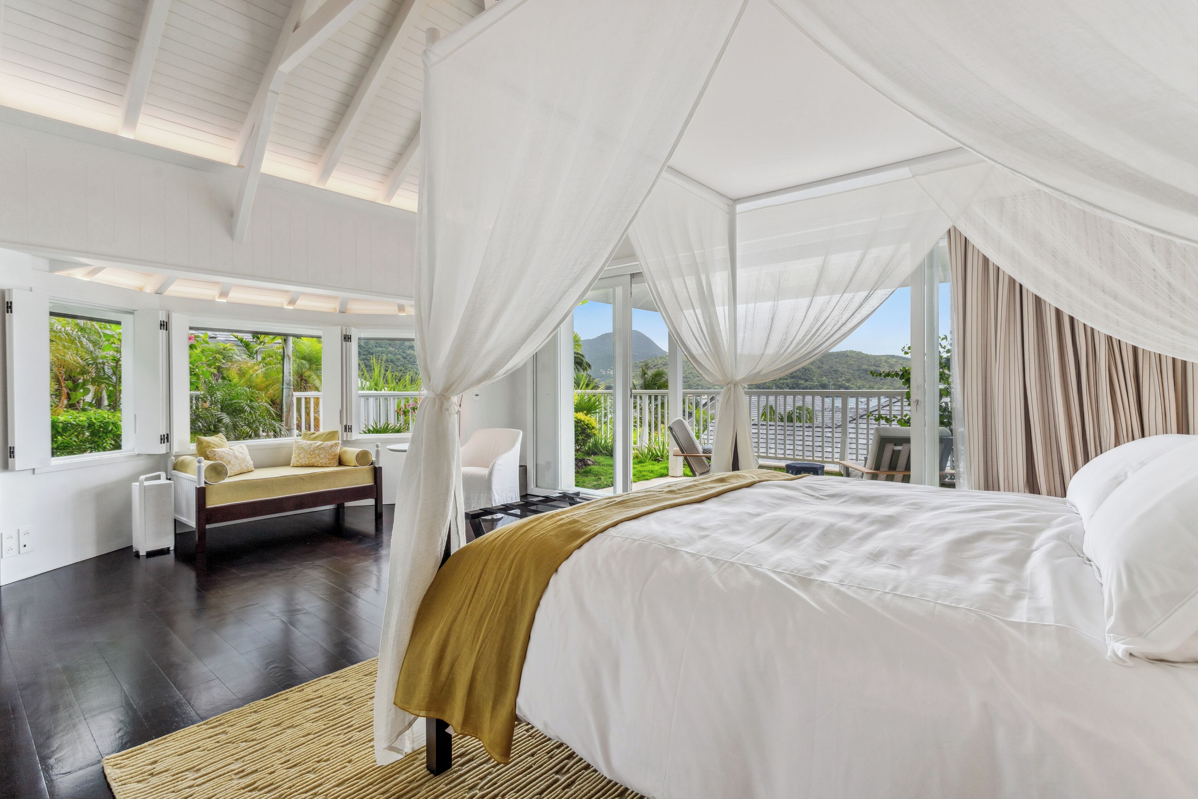 Une chambre spacieuse avec un grand lit, un canapé et une vue sur une végétation luxuriante et des montagnes.