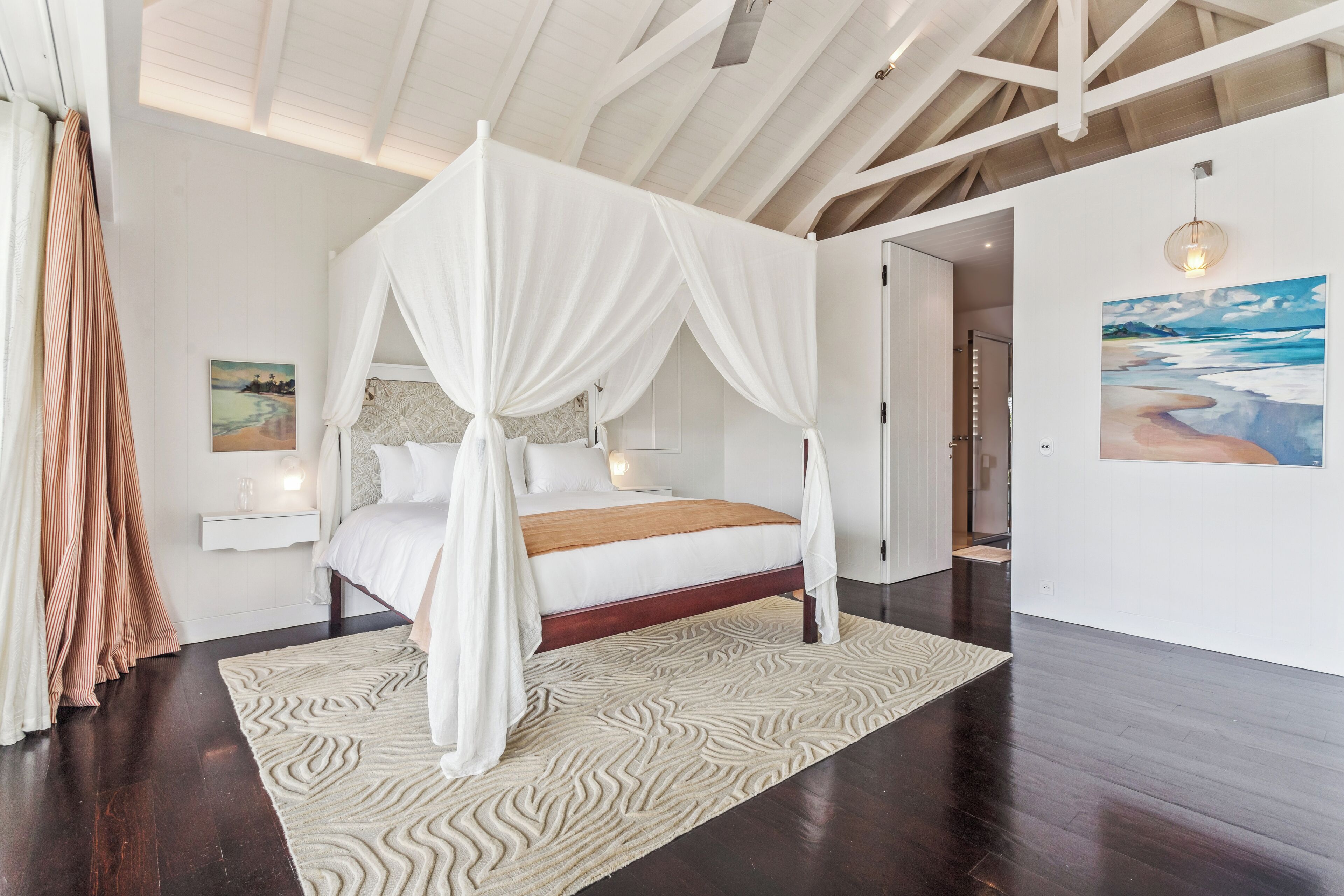 A bedroom with a four-poster bed, a patterned rug, and a painting on the wall.