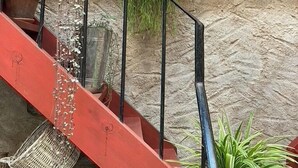 Uma escadaria com corrimão vermelho, grades de metal e plantas em vasos.