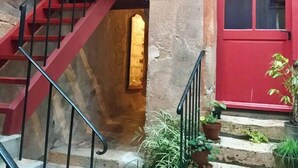 Uma escadaria com corrimãos vermelhos leva a um patamar, onde se vê uma porta vermelha e plantas em vasos.
