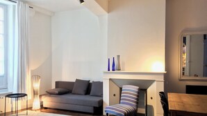 Uma sala de estar moderna com um sofá cinza, uma poltrona listrada, uma mesa de jantar de madeira e uma lareira.