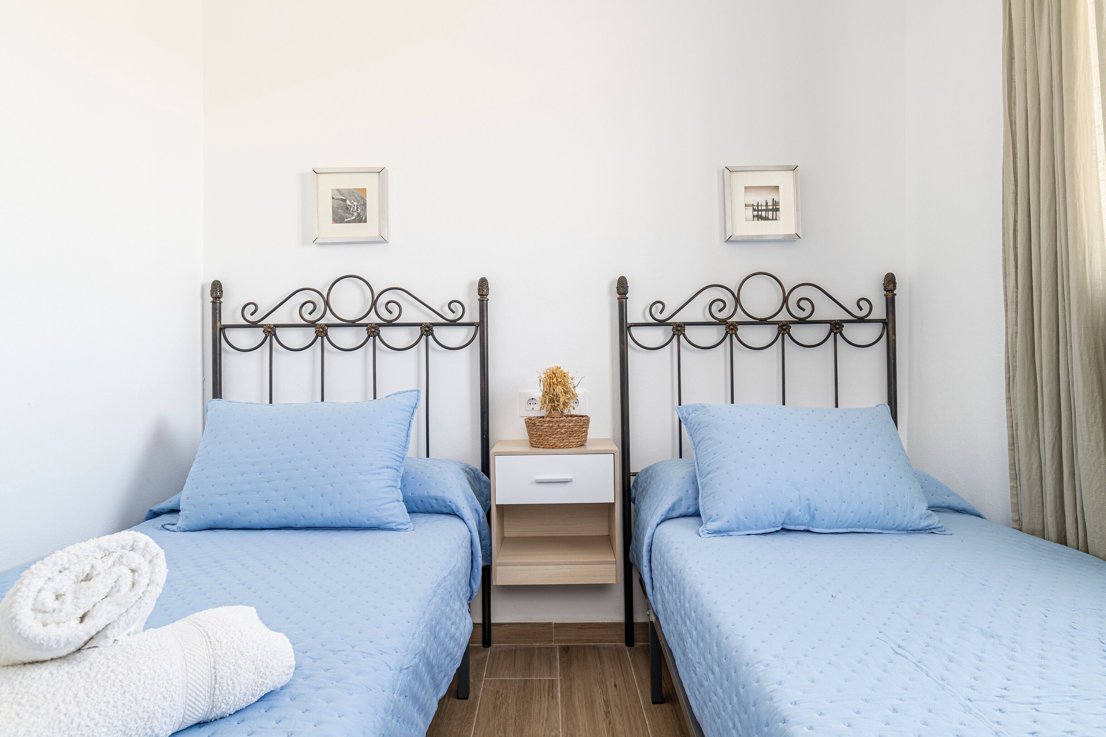 A twin room with two beds, a nightstand, and a wall-mounted shelf.