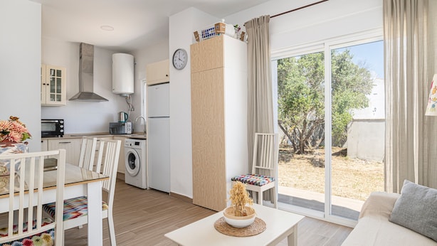 Cocina moderna con horno, microondas y lavadora integrados. Hay un comedor con mesa y sillas, además de un sofá con vistas al jardín.