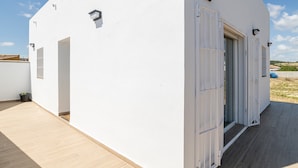 Un edificio blanco con terraza de madera, una puerta y un ventanal pequeño.